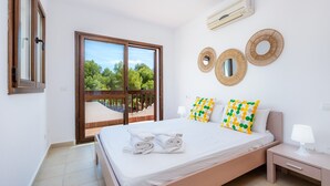 A bedroom with a bed, a nightstand, a window, and a view of greenery.