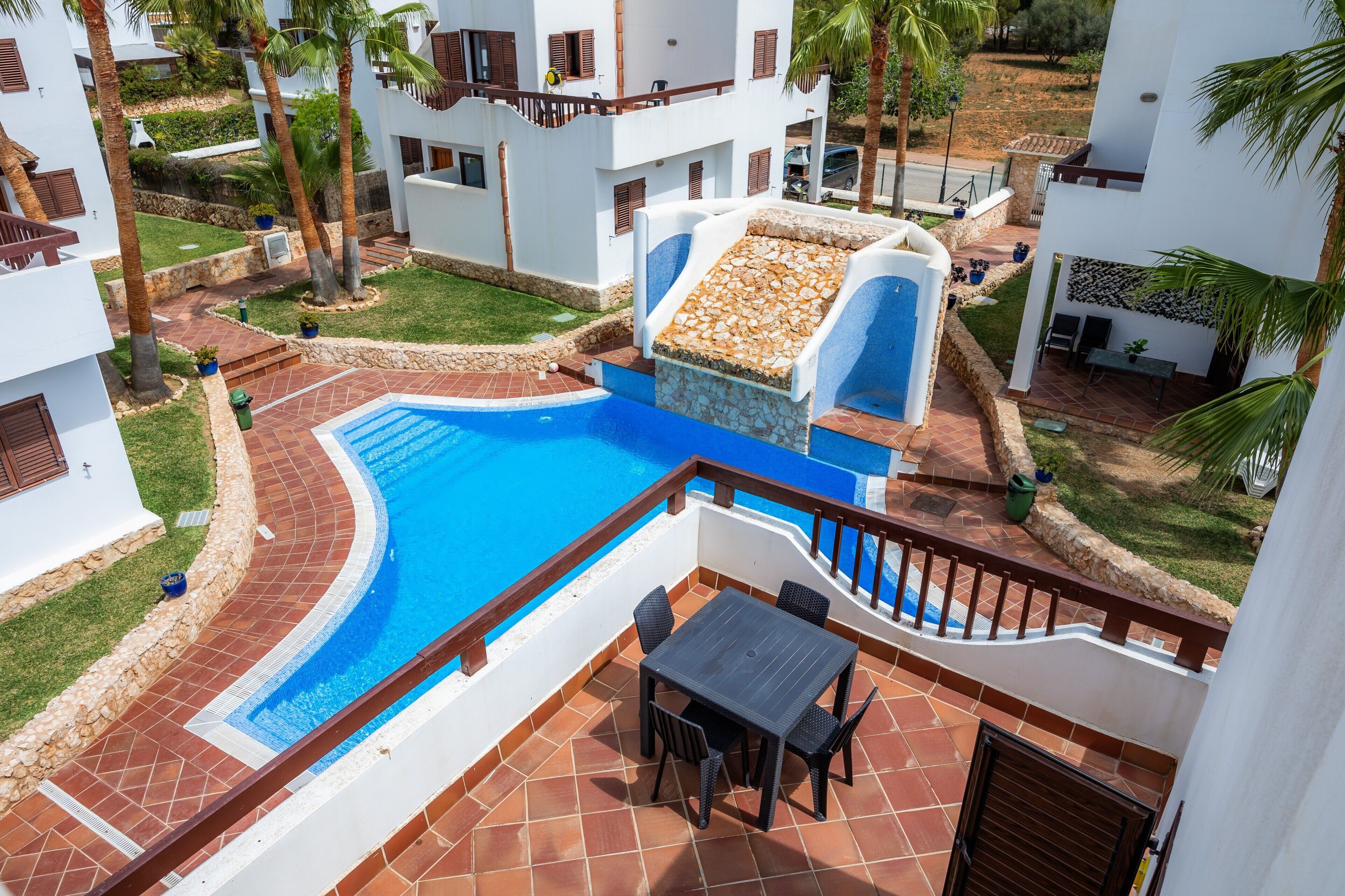 Ein Poolbereich mit einer Terrassentisch und Stühlen, umgeben von weißen Gebäuden mit Balkonen.