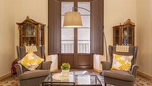 A room with two armchairs, a glass coffee table, a floor lamp, and a window with blinds.