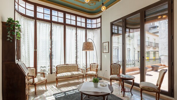 A spacious living room with large windows, a piano, and a balcony with outdoor furniture.