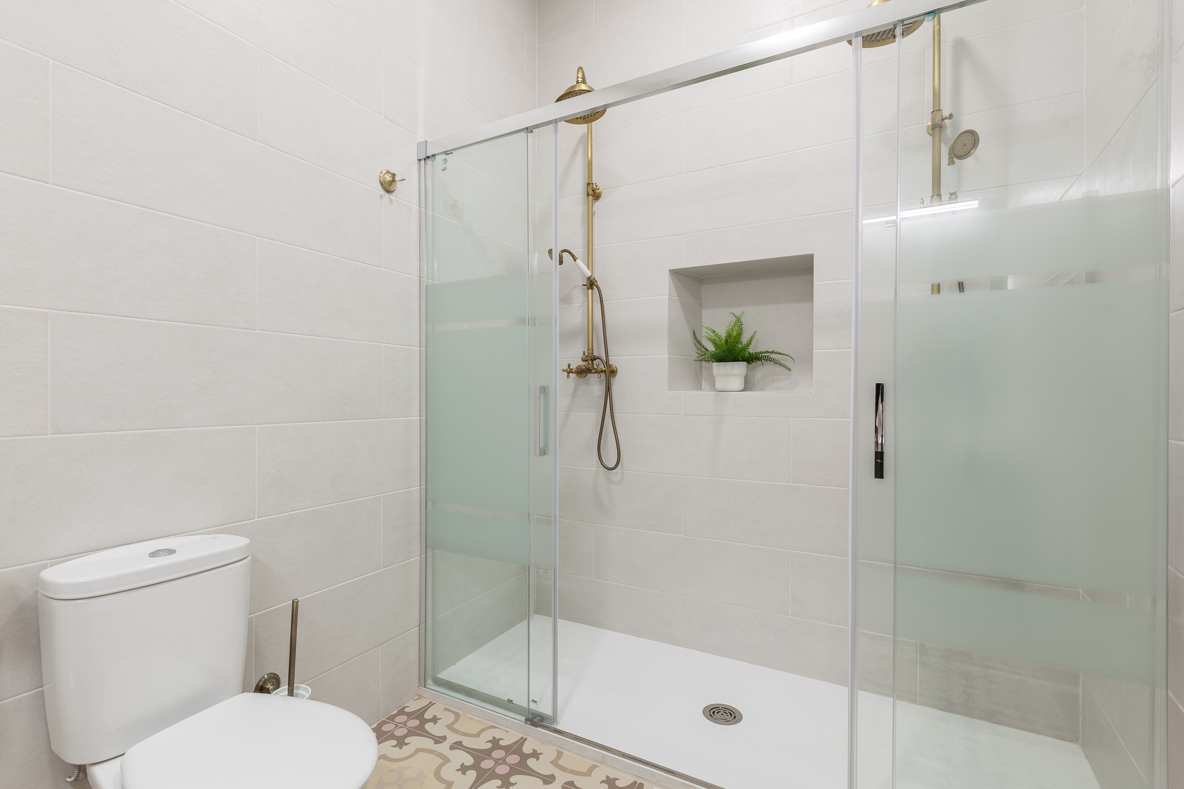 A glass-enclosed shower stall with a white toilet and a small shelf with a plant.