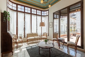 A spacious living room with large windows, a piano, and a balcony with outdoor furniture.