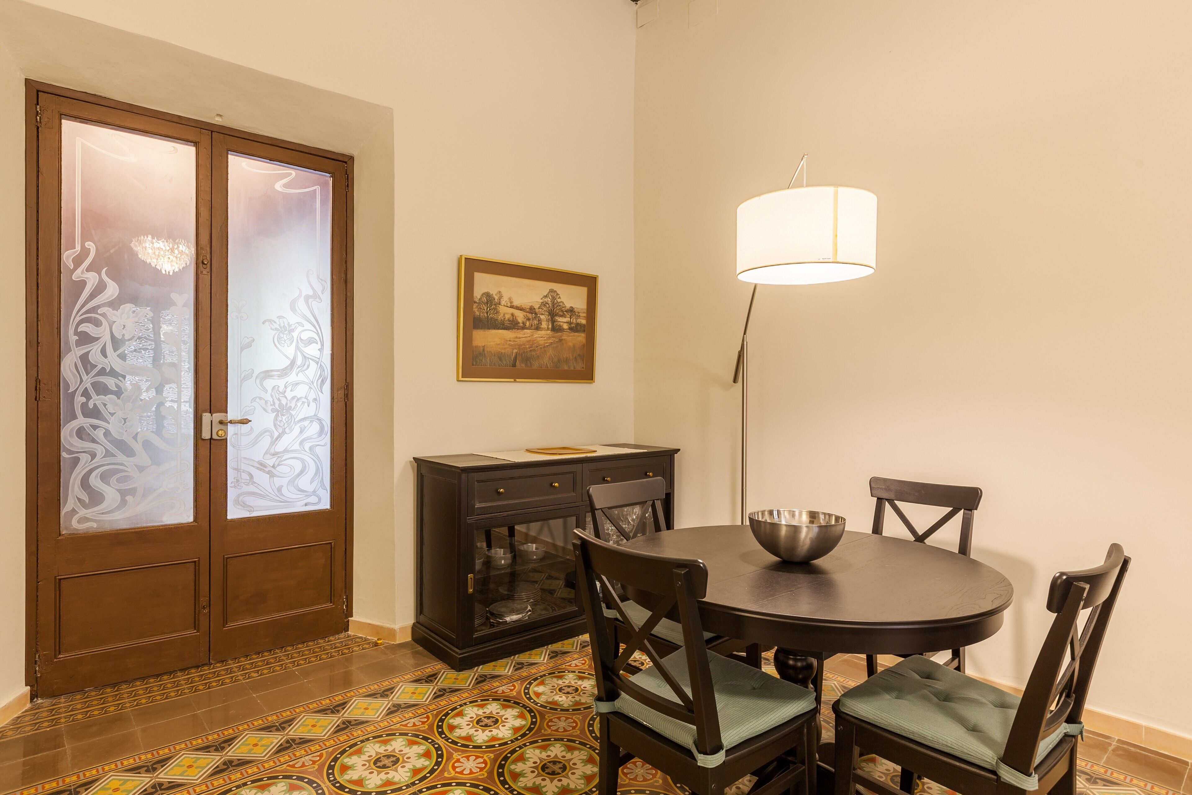 Un coin repas comprenant une table ronde, quatre chaises, un buffet, un tableau et un lampadaire.