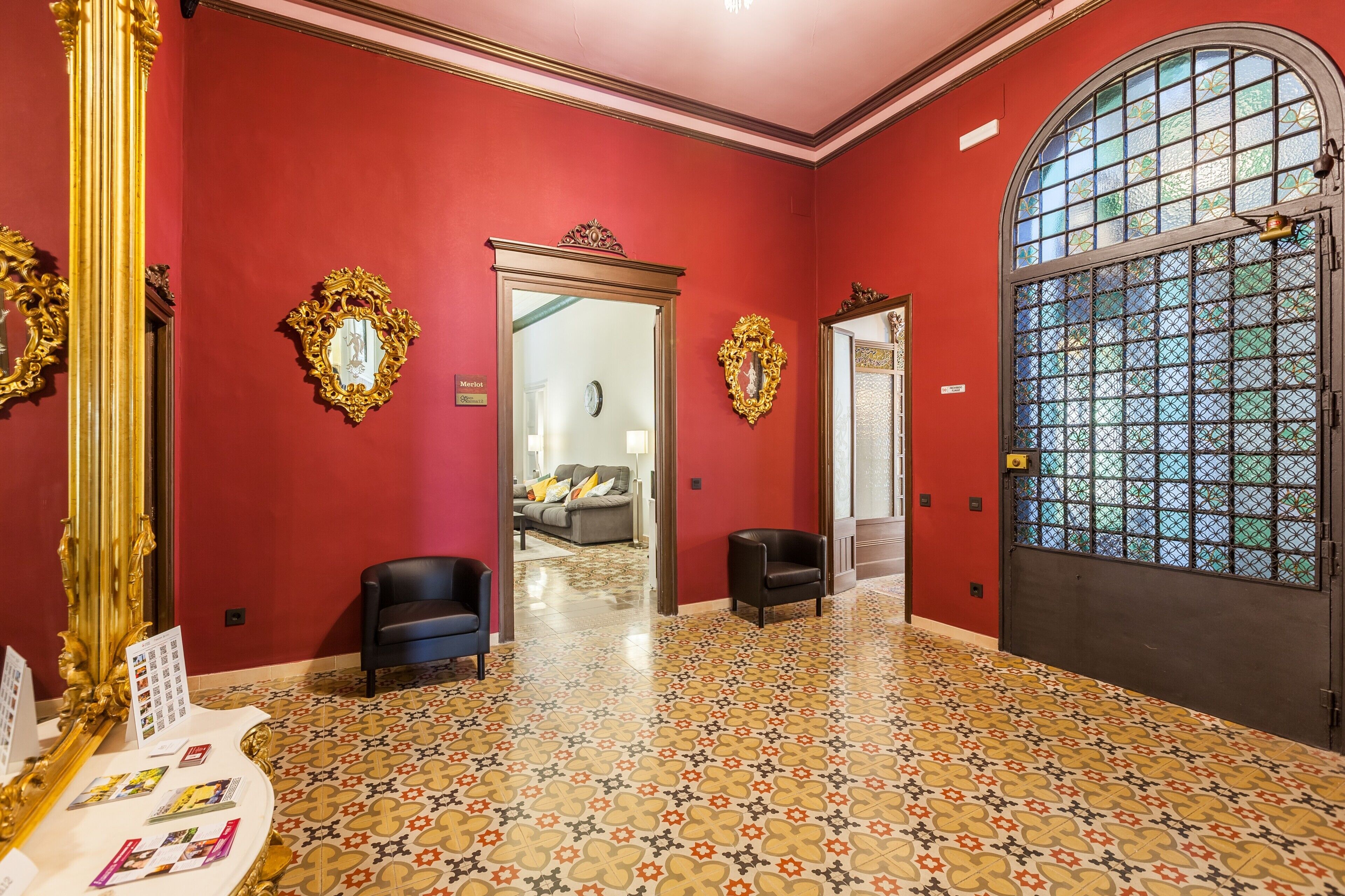 A red-walled room with ornate gold mirrors, a patterned floor, and a large arched window.
