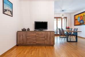 A modern living room with a wooden cabinet, a flat-screen TV, and a dining area with chairs and a table.