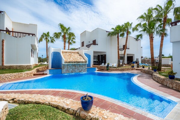 A swimming pool with a slide, palm trees, and a stone border.