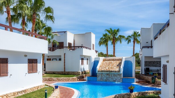 A pool area with a water slide, palm trees, and white buildings with balconies.