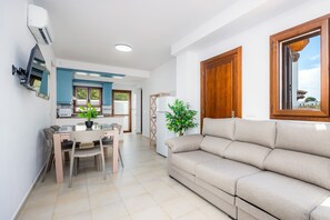 Un salon moderne avec un canapé, une table à manger et des chaises, une plante en pot et une vue par la fenêtre.