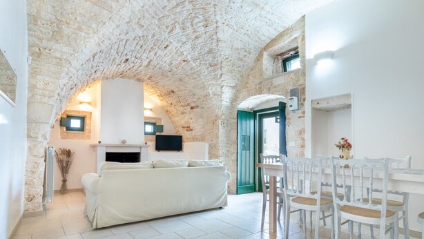 Une pièce avec un canapé blanc, une table à manger avec des chaises, une cheminée et un plafond en pierre.