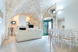 A room with a white sofa, a dining table with chairs, a fireplace, and a stone ceiling. - Holiday Home Casa Maestra with Terrace & Wi-Fi (Ceglie Messapica)