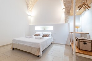 Une chambre à coucher avec un lit, des oreillers, une table de chevet, un miroir et une valise.