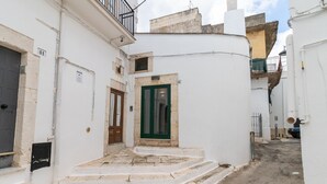 Une rue étroite bordée de bâtiments blancs, avec une porte verte et des marches menant à l’entrée d’un immeuble.