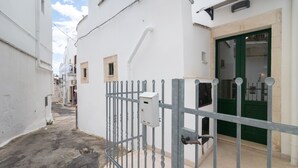 Une rue étroite, avec une entrée fermée par un portail, une porte verte et un bâtiment blanc doté d’une petite fenêtre.
