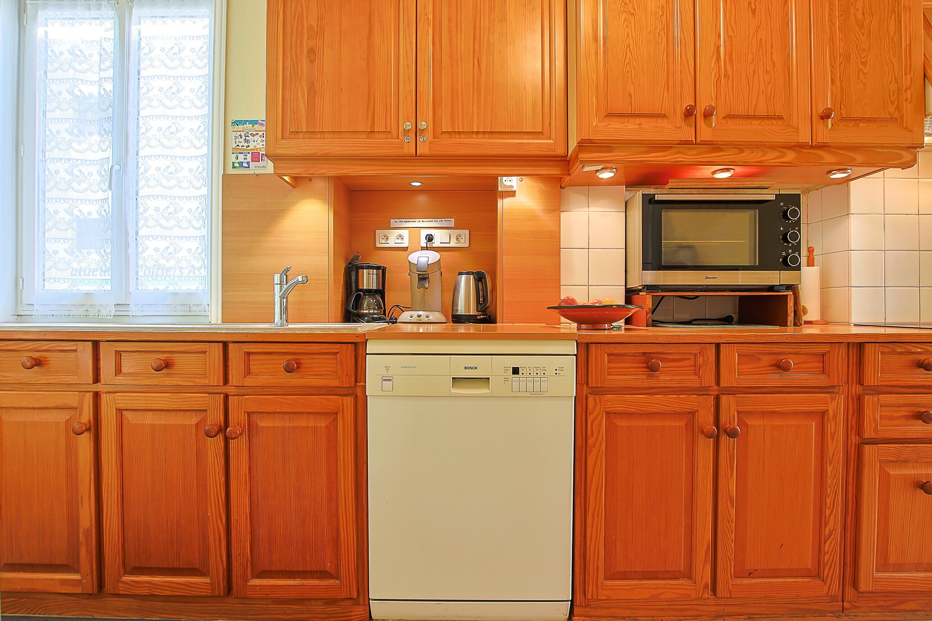 A kitchen with wooden cabinets, a Bosch dishwasher, a microwave, and a coffee maker.