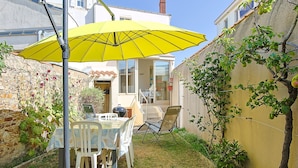 Un patio con una mesa y sillas, un paraguas amarillo y un muro de piedra.