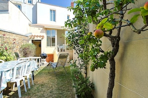 Eine Terrasse mit Tisch und Stühlen, ein kleiner Garten und ein Gebäude mit Fenster und Tür.