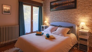 Une chambre à coucher avec un lit, deux tables de chevet avec des lampes, un tableau encadré au mur et une fenêtre avec des rideaux.