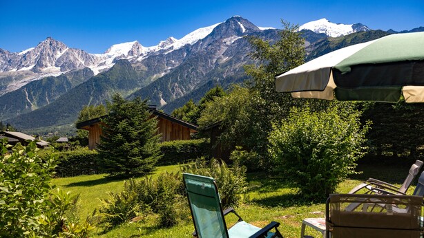 Une vue sur la montagne, avec une cabane en bois, une chaise pliante verte et une table avec un parasol.