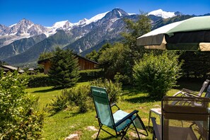 Une vue sur la montagne, avec une cabane en bois, une chaise pliante verte et une table avec un parasol.