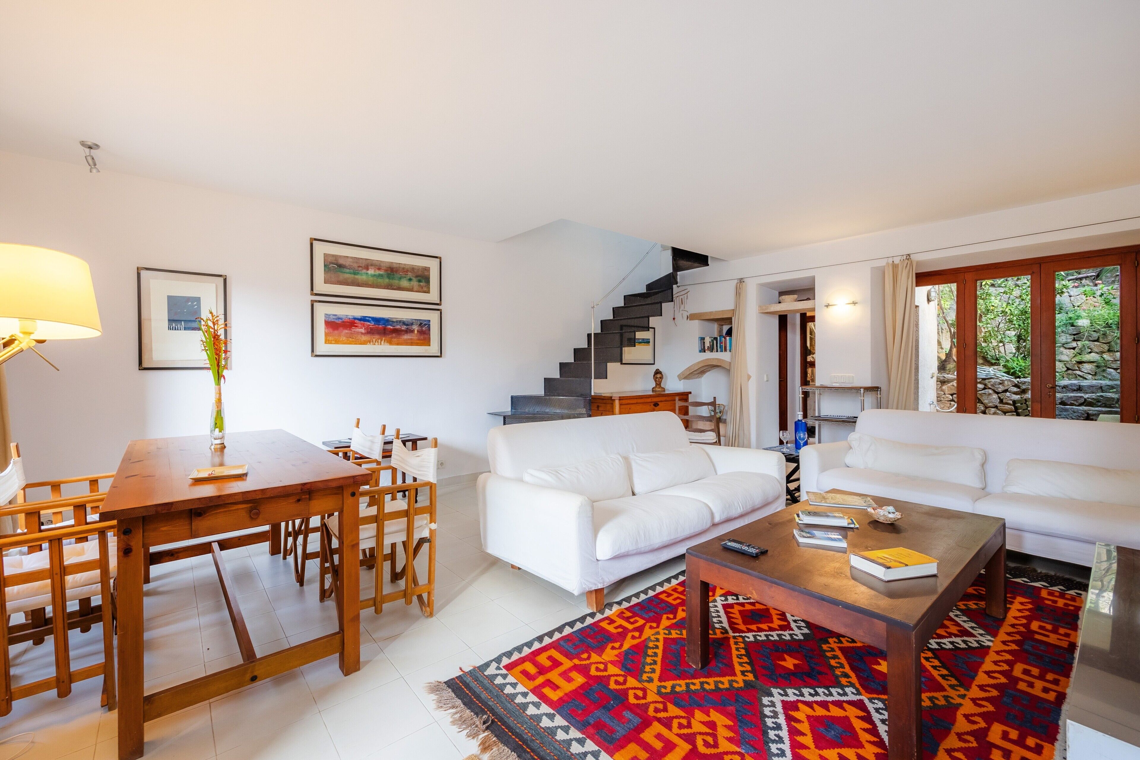 Una sala de estar moderna con un sofá blanco, una mesa de centro de madera y una zona de comedor con una mesa y sillas de madera.