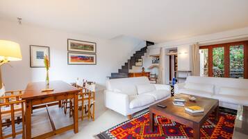 Una sala de estar moderna con un sofá blanco, una mesa de centro de madera y una zona de comedor con una mesa y sillas de madera.