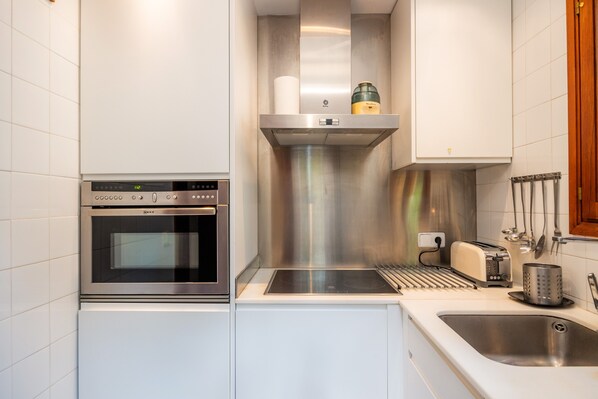 A compact kitchen with a built-in oven, a stainless steel range hood, a toaster, and a sink.