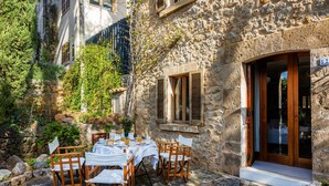 A stone building with a dining area set up outside, featuring a table with chairs and a small garden. - Vacation Home "Casa en Centro Histórico Pollença" with Private Terrace, Garden & Wi-Fi (pollensa)