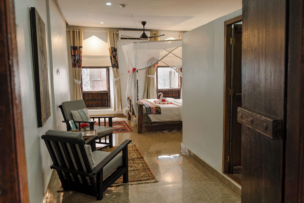 Un pasillo estrecho que conduce a un dormitorio con cama, una silla, una mesa y una ventana con cortinas.