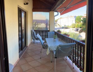 A covered balcony with a table and chairs, potted plants, and a view of the street.