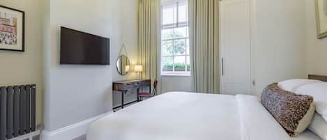 A hotel room with a large bed, a desk with a lamp, a television, and a window with curtains.