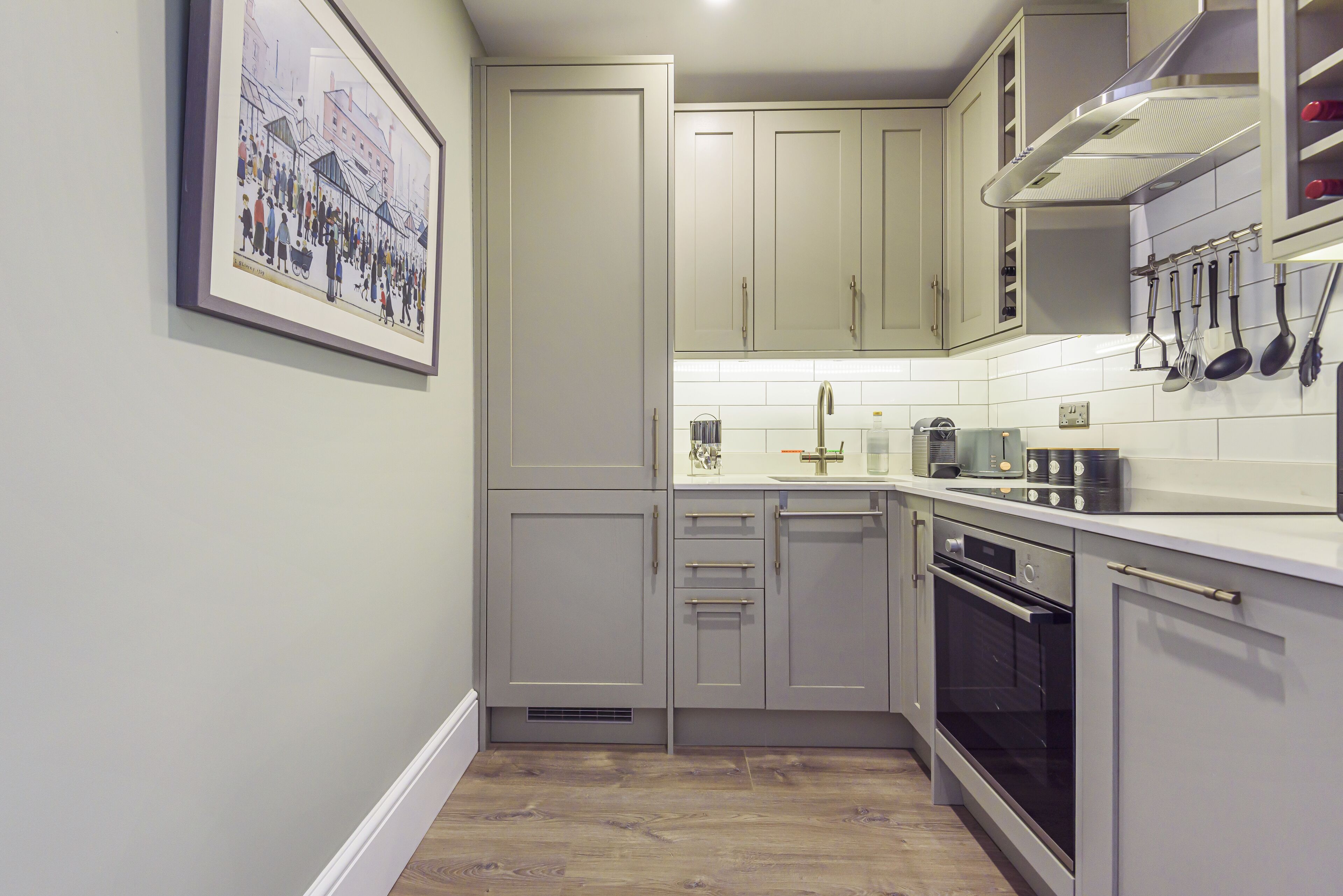 A kitchen with light grey cabinets, a stainless steel oven, and a tiled backsplash.