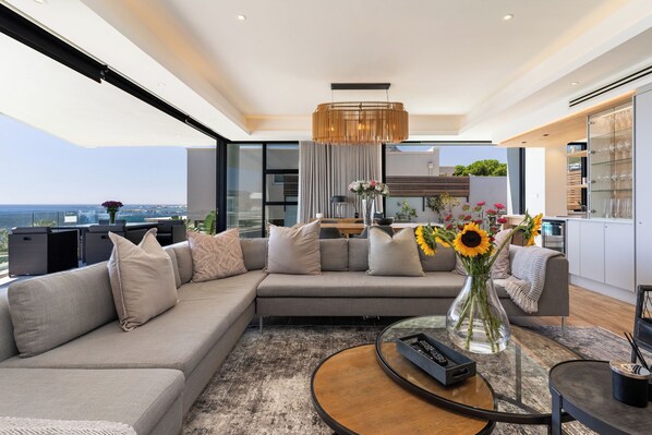 A modern living room with a sectional sofa, a round coffee table, and a view of the sea.