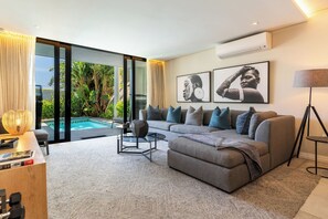 A modern living room with a grey sectional sofa, a glass coffee table, and a pool view.