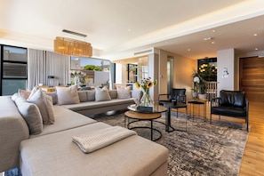 A modern living room with a sectional sofa, a coffee table, and a dining area with chairs. - Little Beach Villa-200m from the beach, best views (Cape Town)