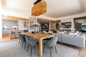 Una sala moderna con una mesa de comedor de madera, sofás grises y un televisor grande.
