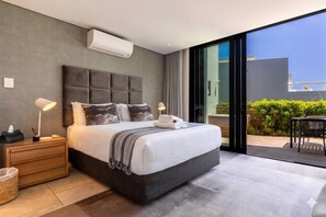 Ein modernes Schlafzimmer mit einem großen Bett, Nachttischlampen, einer integrierten Klimaanlage und einer Schiebetür zu einem Außenbereich.