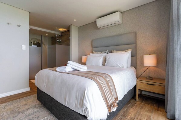 Habitación de hotel con una cama grande, lámparas de noche, un equipo de aire acondicionado y vistas al baño.