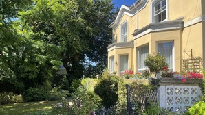 Ein zweistöckiges Gebäude mit Garten, Steinmauern und verschiedenen Pflanzen und Blumen.