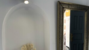 Een witte, gewelfde nis met een koraaldecoratie, een zwarte deur en een spiegel met gouden lijst.