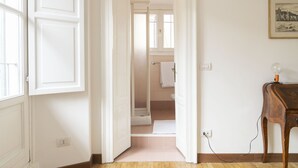 A hallway with a wooden floor, white walls, and a door leading to a bathroom.