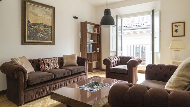 A living room with a brown sofa set, a wooden bookshelf, and a large painting on the wall.