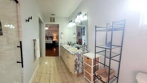 A bathroom with a shower, a sink, and a mirror. There is a shelf with storage bins and a towel rack.