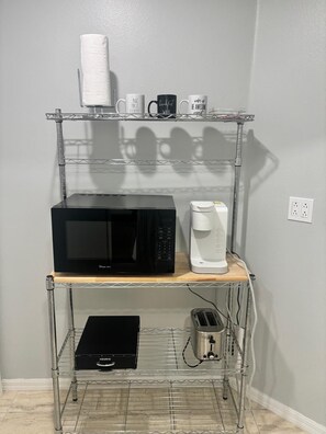 A kitchen area with a metal shelf holding a microwave, coffee maker, and a box labeled 'KEURIG'. - #11 The Paradise  in-law Suite by Joyful Moments (Tampa)