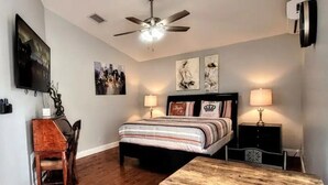 A bedroom with a bed, bedside tables, a desk, a chair, a ceiling fan, and wall art.