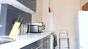 Moderni keittiö, jossa on valkoinen työtaso, ruostumattomasta teräksestä valmistetut kodinkoneet ja valkoinen jääkaappi.