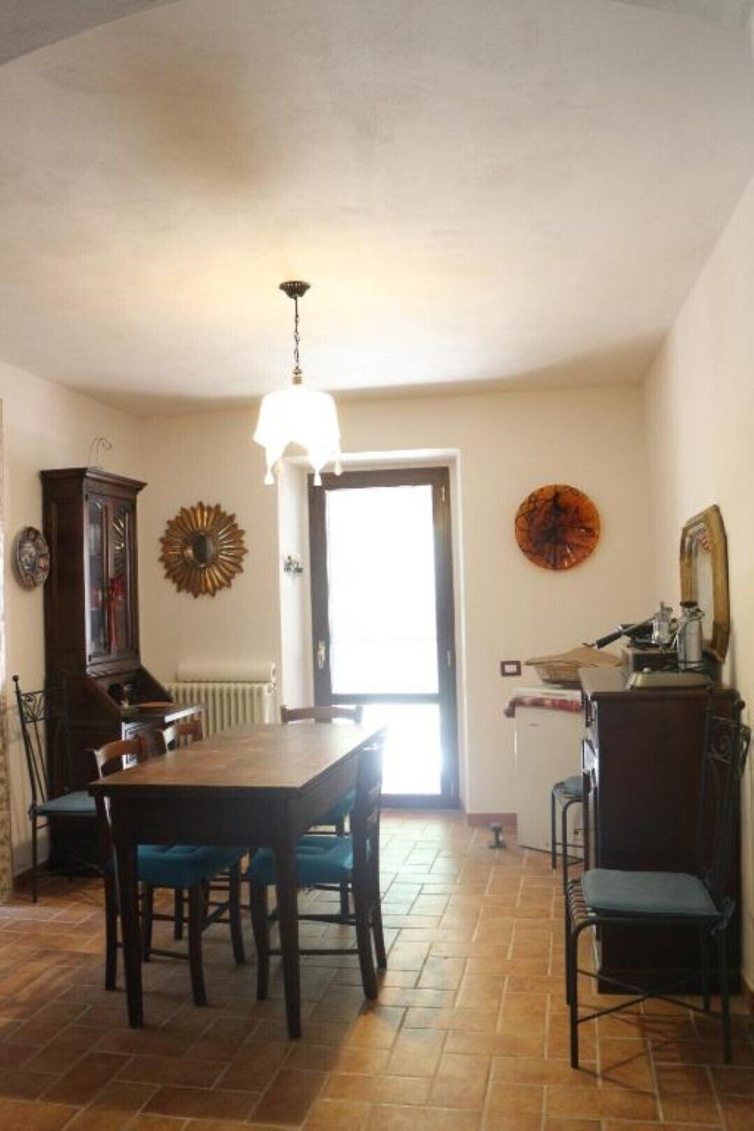 A dining area with a wooden table and chairs, a radiator, and a door leading outside.