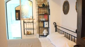 Ein Schlafzimmer mit Steinwand, einem Bett mit weißer Bettwäsche, einem Holz-Kopfschild und einem kleinen Bücherregal.