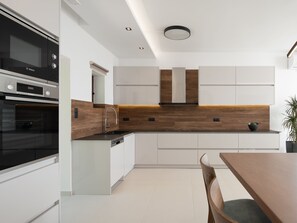 Une cuisine moderne avec des meubles blancs, un four Bosch et un pare-feu en bois.