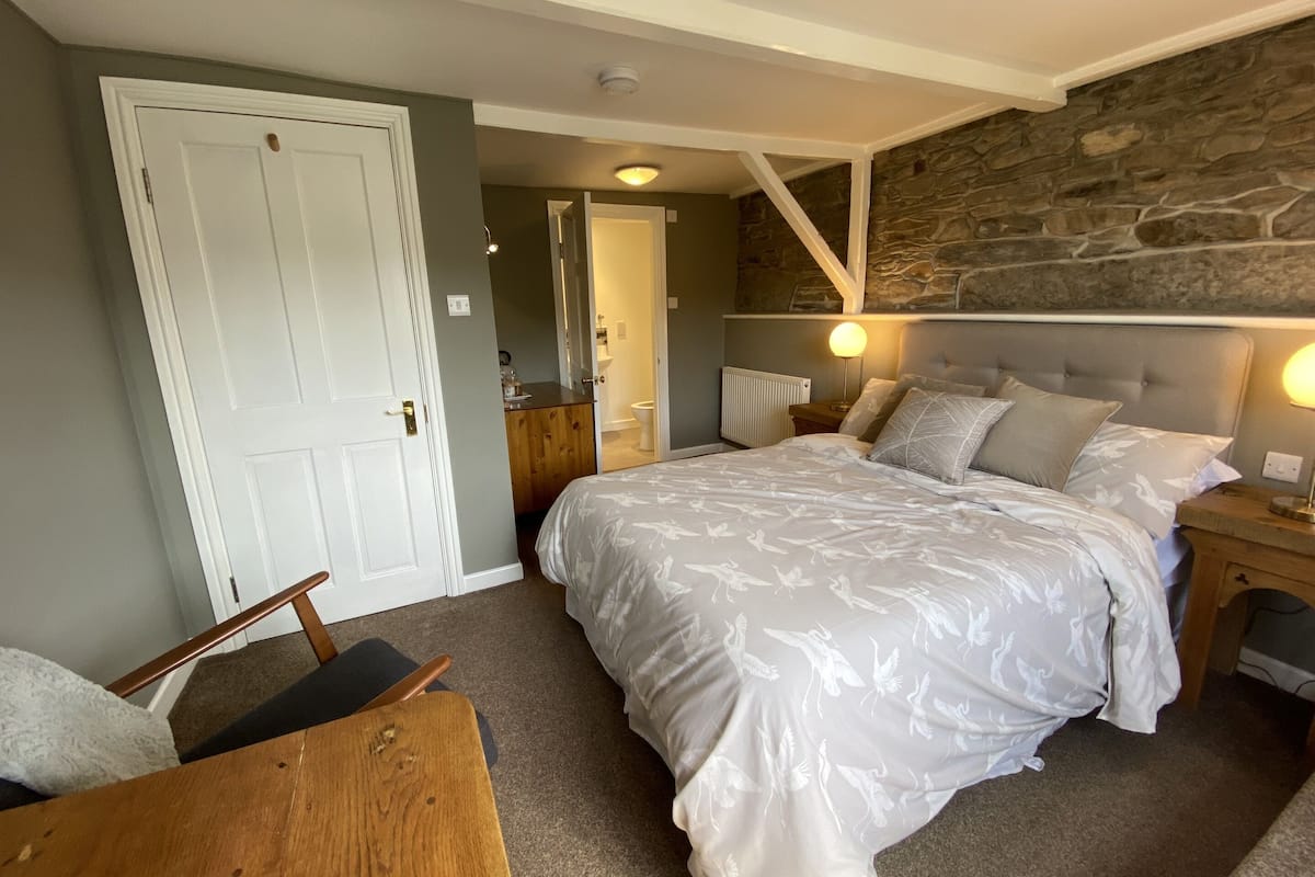 Une chambre avec un grand lit, une chaise en bois, une table de chevet et un mur en pierre.