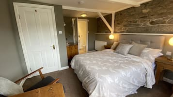 A bedroom with a large bed, a wooden chair, a nightstand, and a stone wall.